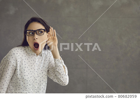Woman with a shocked expression holds her hand to her ear and overhears the conversation. 80682059
