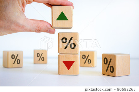 Interest rates symbol. Wooden cubes, businessman changed the direction of an arrow symbolizing that the interest rates are going down or up. Beautiful white background. Business concept. Copy space. Interest rates symbol. Wooden cubes, businessman changed the direction of an arrow symbolizing that the interest rates are going down or up. Beautiful white background. Business concept. Copy space. 80682263