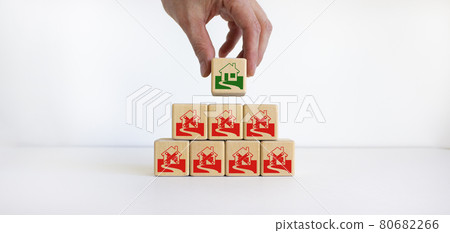 Businessman placing a cube with house sign near of a other cubes. Cubes with abandoned house icons. The concept of overcoming the crisis. Beautiful white background. Businessman placing a cube with house sign near of a other cubes. Cubes with abandoned house icons. The concept of overcoming the crisis. Beautiful white background. 80682266