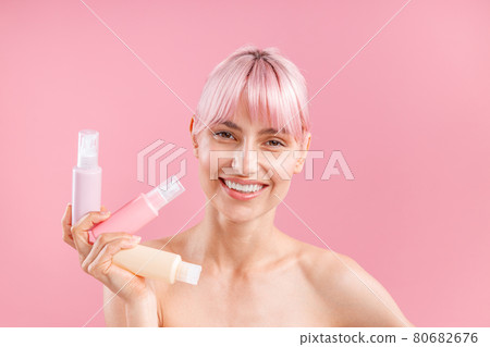 Happy young woman with pink hair holding three plastic travel bottles with beauty products, posing isolated over pink background Happy young woman with pink hair holding three plastic travel bottles with beauty products, posing isolated over pink background 80682676