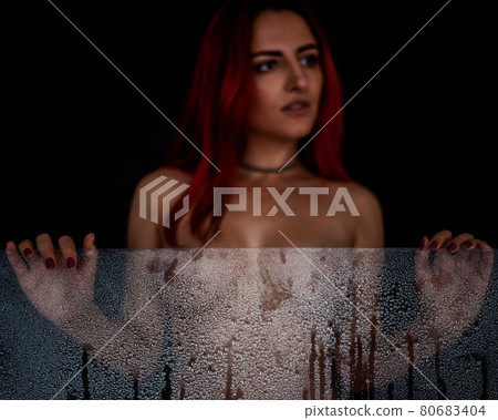 Beautiful naked woman holding a misted glass in her hands in drops of water. Focus on the glass. Black background Beautiful naked woman holding a misted glass in her hands in drops of water. Focus on the glass. Black background 80683404