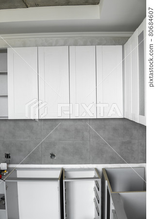 Custom kitchen cabinets installation with a white furniture facades mdf. Gray modular kitchen from chipboard material on a various stages of installation. A frame furniture fronts mdf profile. 80684607