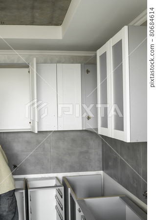 Custom kitchen cabinets installation with a white furniture facades mdf. Gray modular kitchen from chipboard material on a various stages of installation. A frame furniture fronts mdf profile. 80684614