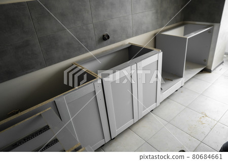 Lower custom kitchen cabinets installation with a furniture facades mdf. Gray modular kitchen from chipboard material on a various stages of installation. A frame furniture fronts mdf profile. Lower custom kitchen cabinets installation with a furniture facades mdf. Gray modular kitchen from chipboard material on a various stages of installation. A frame furniture fronts mdf profile. 80684661