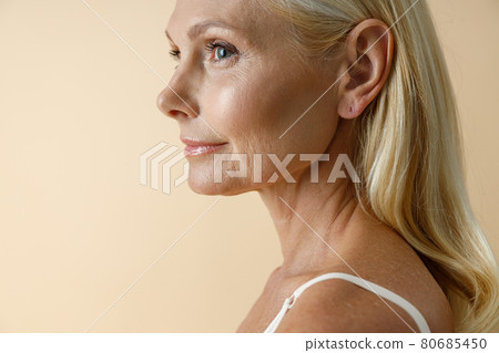 Close up portrait of mature blonde woman in white underwear looking away, posing isolated over beige background Close up portrait of mature blonde woman in white underwear looking away, posing isolated over beige background 80685450