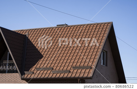 Brown corrugated metal profile roof installed on a modern house. The roof of corrugated sheet. Roofing of metal profile wavy shape. Modern roof made of metal. Metal roofing. Brown corrugated metal profile roof installed on a modern house. The roof of corrugated sheet. Roofing of metal profile wavy shape. Modern roof made of metal. Metal roofing. 80686522