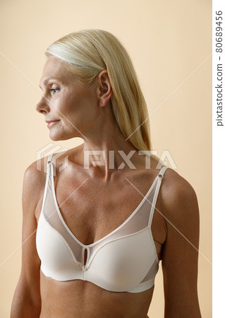 Portrait of beautiful mature blonde woman in white bra posing with eyes closed isolated over beige background Portrait of beautiful mature blonde woman in white bra posing with eyes closed isolated over beige background 80689456