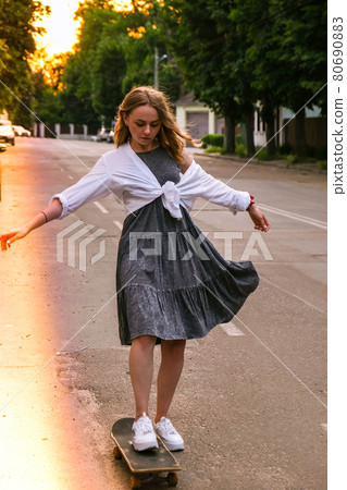 Millennial Woman in dress riding a skateboard on street. Skater girl on a longboard. Cool female skateboarder at sunset. Carefree female skater 20s enjoying freedom youth lifestyle Hobby Millennial Woman in dress riding a skateboard on street. Skater girl on a longboard. Cool female skateboarder at sunset. Carefree female skater 20s enjoying freedom youth lifestyle Hobby 80690883