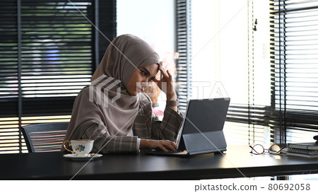 A muslim businesswoman in hijab is  tired from work while sitting in the office. 80692058