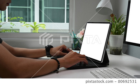 Cropped shot of concentrated young man freelancer is typing on computer tablet with blank screen while sitting at working place. Cropped shot of concentrated young man freelancer is typing on computer tablet with blank screen while sitting at working place. 80692531