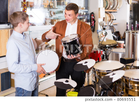 teenager and father deciding on drum unit in musical shop 80693551