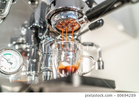 Coffee maching making espresso shot in naked bottomless portafilter at home kitchen. Beautiful crema pouring in transparent double wall glass Coffee maching making espresso shot in naked bottomless portafilter at home kitchen. Beautiful crema pouring in transparent double wall glass 80694289