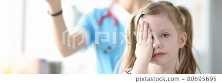 Little girl covering her eyes with her hand at ophthalmologist appointment Little girl covering her eyes with her hand at ophthalmologist appointment 80695695