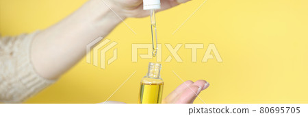Female hands holding bottle of cosmetic oil on yellow background closeup Female hands holding bottle of cosmetic oil on yellow background closeup 80695705
