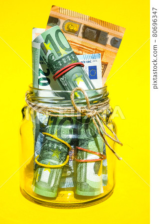 Glass jars filled with Euro bills, savings inside glass jar, money isolated on yellow background, copy space for text. Paper note. Business budget of wealth Glass jars filled with Euro bills, savings inside glass jar, money isolated on yellow background, copy space for text. Paper note. Business budget of wealth 80696347