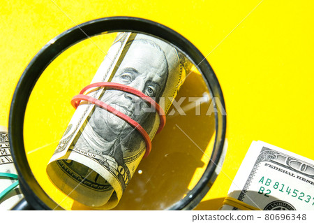 Magnifying glass on the background of a bundle of dollars close-up, one hundred dollars franklin, one thousand texture, background. Business budget of wealth 80696348