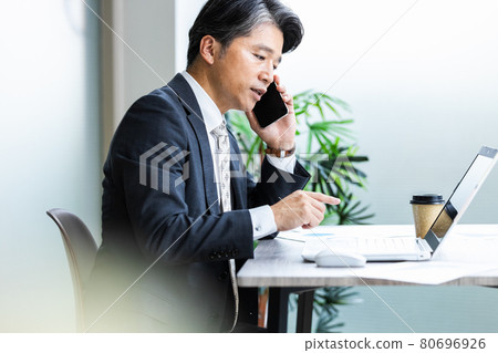 A businessman talking on a smartphone while looking at the computer screen A businessman talking on a smartphone while looking at the computer screen 80696926