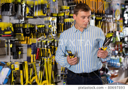 Happy male customer examining secateurs in garden equipment shop 80697893