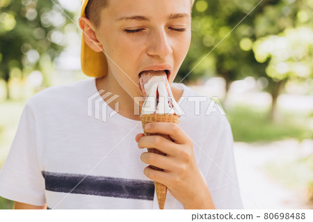 Teenager boy eating ice-cream cone on green nature background. Summer, junk food and people concept 80698488
