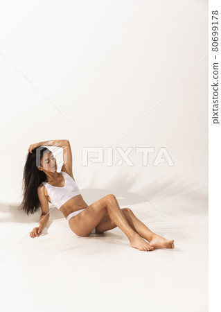 Portrait of young beautiful tanned woman in white underwear lying on floor over white background. Portrait of young beautiful tanned woman in white underwear lying on floor over white background. 80699178