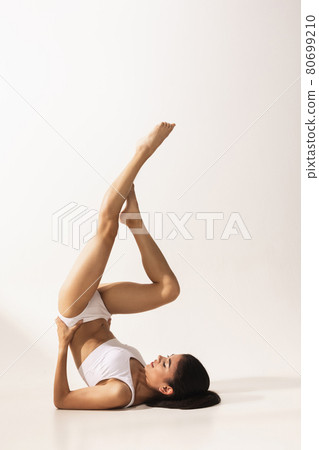 Portrait of young beautiful tanned woman in white underwear lying on floor over white background. Portrait of young beautiful tanned woman in white underwear lying on floor over white background. 80699210