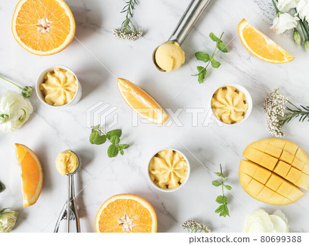 Orange and mango sorbet in bowl and in ice cream spoons and fruits spices on marble background. Orange and mango sorbet in bowl and in ice cream spoons and fruits spices on marble background. 80699388