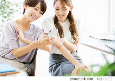 兩名女商人一邊看著智能手機，一邊與後座的同事交談 80699988