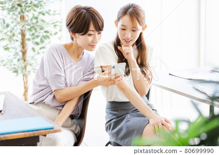 Two business women talking with a colleague in the back seat while looking at a smartphone 80699990