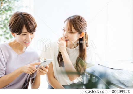 Two business women talking with a colleague in the back seat while looking at a smartphone Two business women talking with a colleague in the back seat while looking at a smartphone 80699998