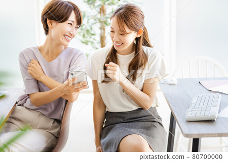 兩名女商人一邊看著智能手機,一邊與後座的同事交談 兩名女商人一邊看著智能手機,一邊與後座的同事交談 80700000