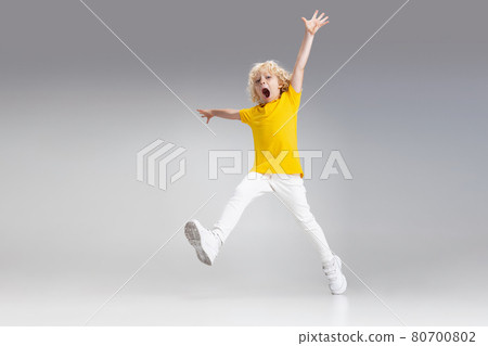 Cute little curly preschool boy having fun, playing isolated over light studio background. 80700802