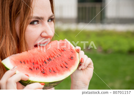 Close-up portrait of red-haired young woman with braces eating watermelon outdoors 80701157