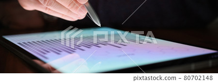 Male hand holds stylus over screen of tablet with commercial charts in dark 80702148