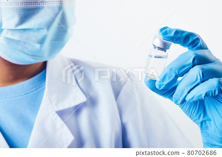 Closeup vial of covid-19 vaccine in hand of professional scientist or doctor in laboratory for treatment with mask gloves and lab coat on white background. Health business and industry concept. Closeup vial of covid-19 vaccine in hand of professional scientist or doctor in laboratory for treatment with mask gloves and lab coat on white background. Health business and industry concept. 80702686