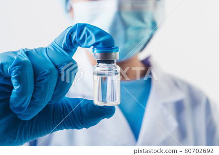 Closeup vial of covid-19 vaccine in hand of professional scientist or doctor in laboratory for treatment with mask gloves and lab coat on white background. Health business and industry concept. Closeup vial of covid-19 vaccine in hand of professional scientist or doctor in laboratory for treatment with mask gloves and lab coat on white background. Health business and industry concept. 80702692