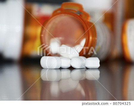 Pills spilling out of a prescription drug bottle and reflecting on a counter 80704325