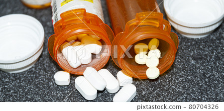 Pills spilling out of two prescription pill bottles on a black counter 80704326