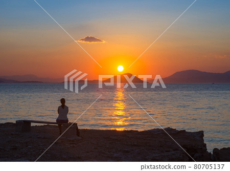 Girl silhouette watching the sunset over the Mediterranean Sea from the Aegina island in Saronic gulf, Greece. Girl silhouette watching the sunset over the Mediterranean Sea from the Aegina island in Saronic gulf, Greece. 80705137