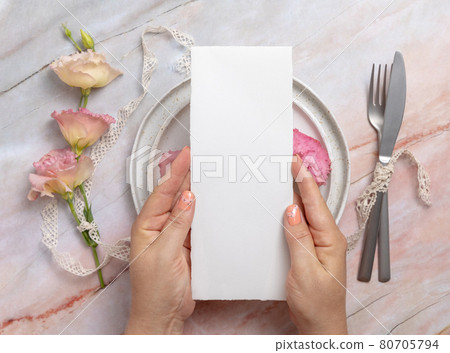 Hands holding wedding menu over a ceramic plate on a marble table 80705794
