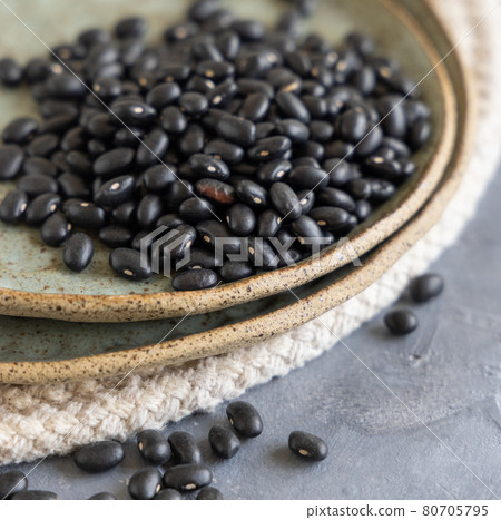 Ceramic plate full of dry black beans on grey table closeup 80705795