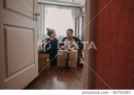 Moving day celebration. Yong couple Move Into New Home. Young happy couple, newlyweds family drinking wine and having fun in room with carton boxes in new home 80705985