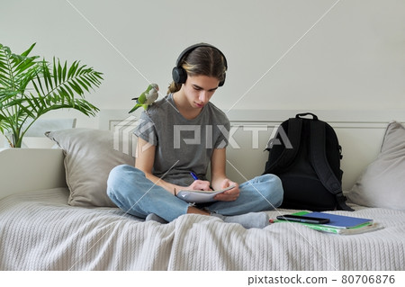 Male teenager with pet parrot, guy student sitting in headphones at home 80706876