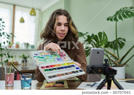 Teenage guy drawing with watercolors, watching video class on smartphone Teenage guy drawing with watercolors, watching video class on smartphone 80707091