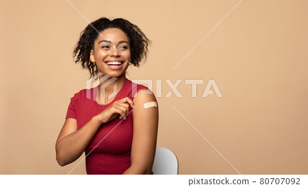 Cheerful vaccinated black woman showing arm with bandage after coronavirus vaccine injection on beige background Cheerful vaccinated black woman showing arm with bandage after coronavirus vaccine injection on beige background 80707092