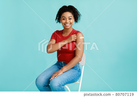 Covid-19 vaccination campaign. Black female patient showing arm with adhesive bandage after coronavirus vaccine 80707119