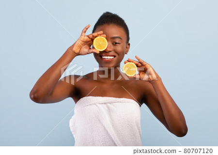 Excited african american lady with lemon halves in hands, posing wrapped in towel over blue background 80707120