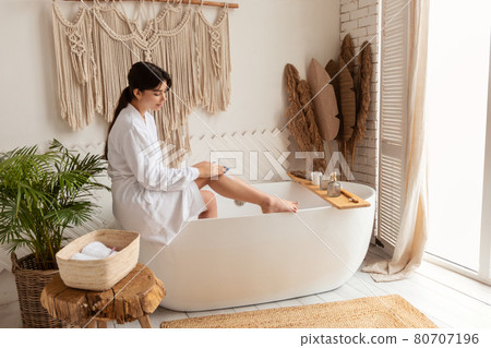 Side-View Of Woman Applying Depilation Cream On Legs In Bathroom 80707196