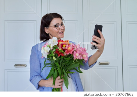 Happy middle-aged woman with large bouquet of flowers and smartphone 80707662