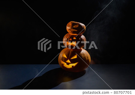 A spooky pyramid of jack-o-lantern in the dark. Glowing scary smirk carved in a pumpkin. Traditional halloween decorations. Horizontal greeting card or banner. 80707701