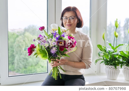 Portrait of beautiful mature woman with bouquet at home 80707998